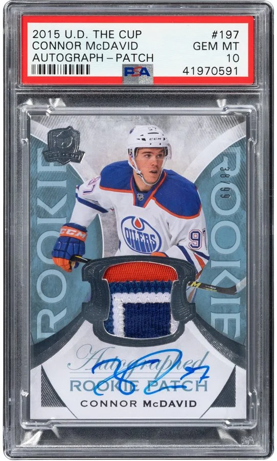 2015 U.D. The Cup hockey trading card of Connor McDavid, graded GEM MT 10, featuring a patch of his jersey and autograph, encased in a plastic slab with a PSA label.