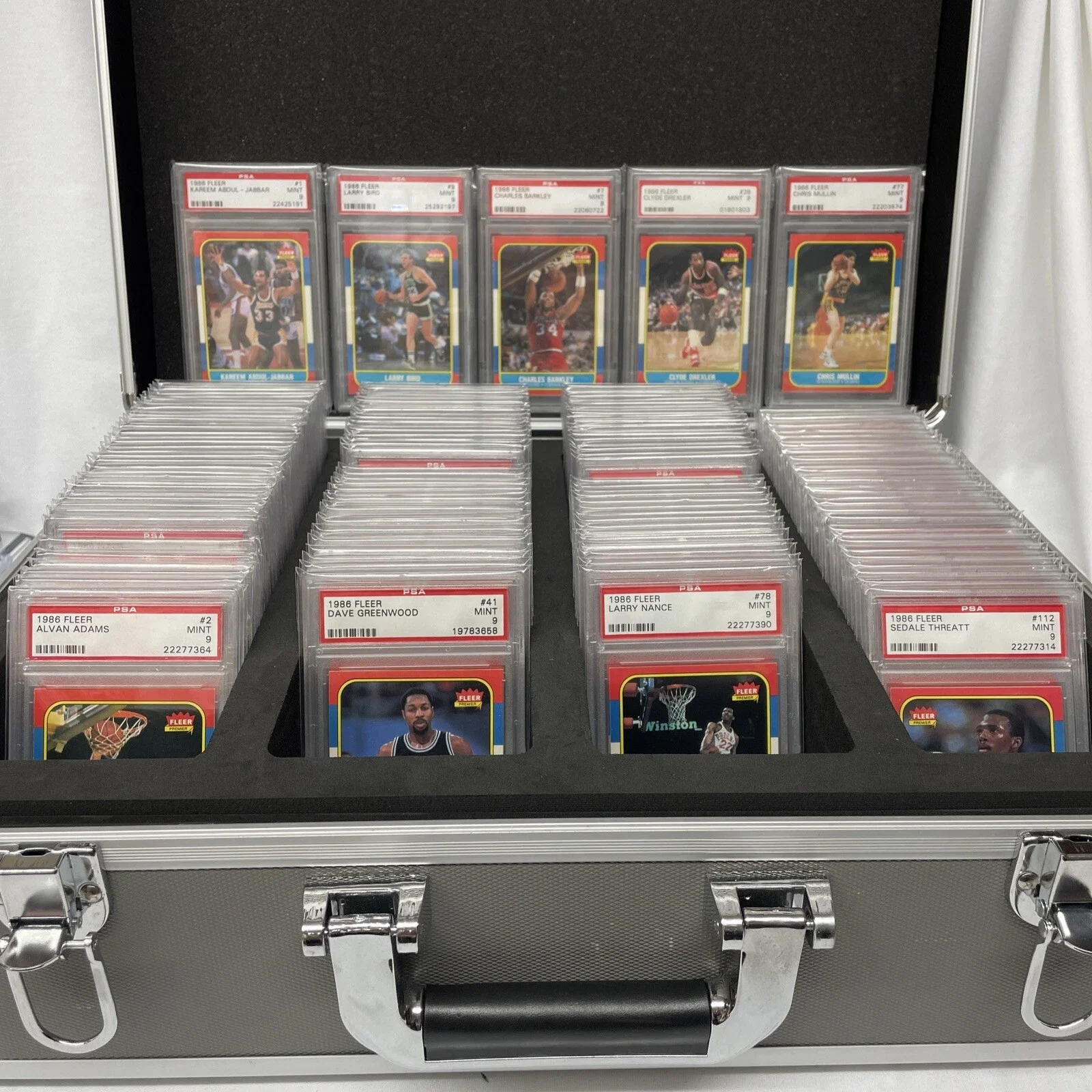 Collection of 1986 Fleer basketball trading cards in a display case, featuring players such as Kareem Abdul-Jabbar, Larry Bird, Charles Barkley, Clyde Drexler, and Chris Mullin.