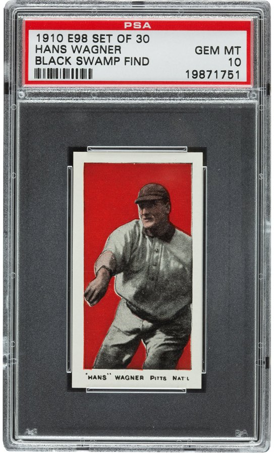 A PSA graded 1910 E98 set of 30 baseball card featuring Hans Wagner with a red background, stored in a protective case. The label states it's a Black Swamp Find, graded GEM MT 10.