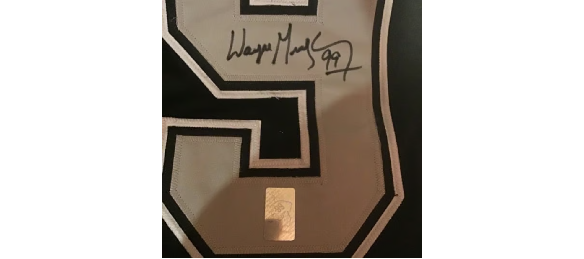 A black and white sports jersey with a large number '9' on it. The jersey has an autograph signed in black marker, reading 'Wayne M. 99'.
