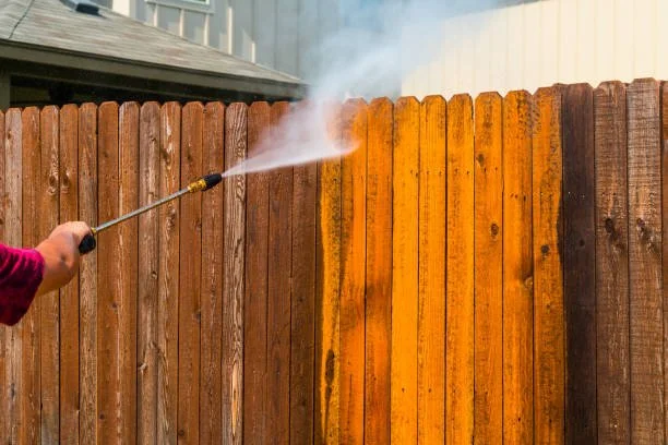 Person using a pressure washer to clean a wooden fence.