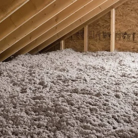 Insulation material evenly spread on the floor of an unfinished attic with a sloped wooden ceiling.