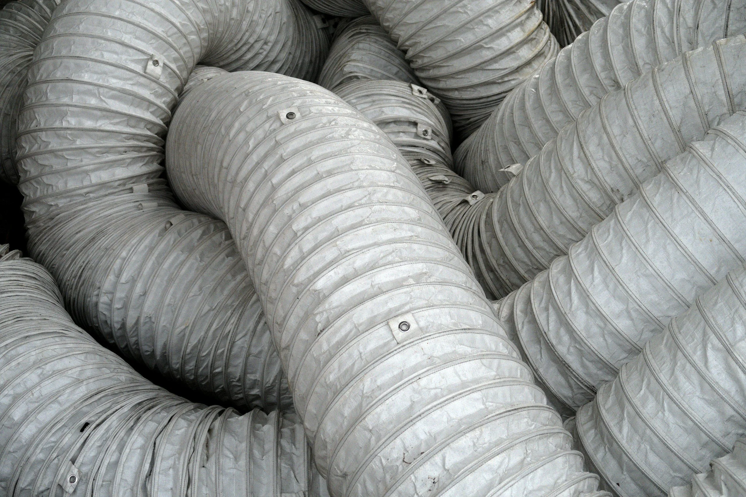 A large number of white, flexible plastic ducts or hoses are stacked together in a pile.