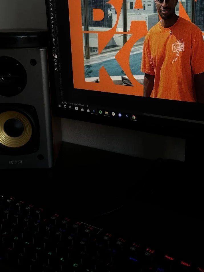 Imagem mostrando uma tela de computador com uma foto de uma pessoa usando uma camiseta laranja, e uma caixa de som ao lado da tela.