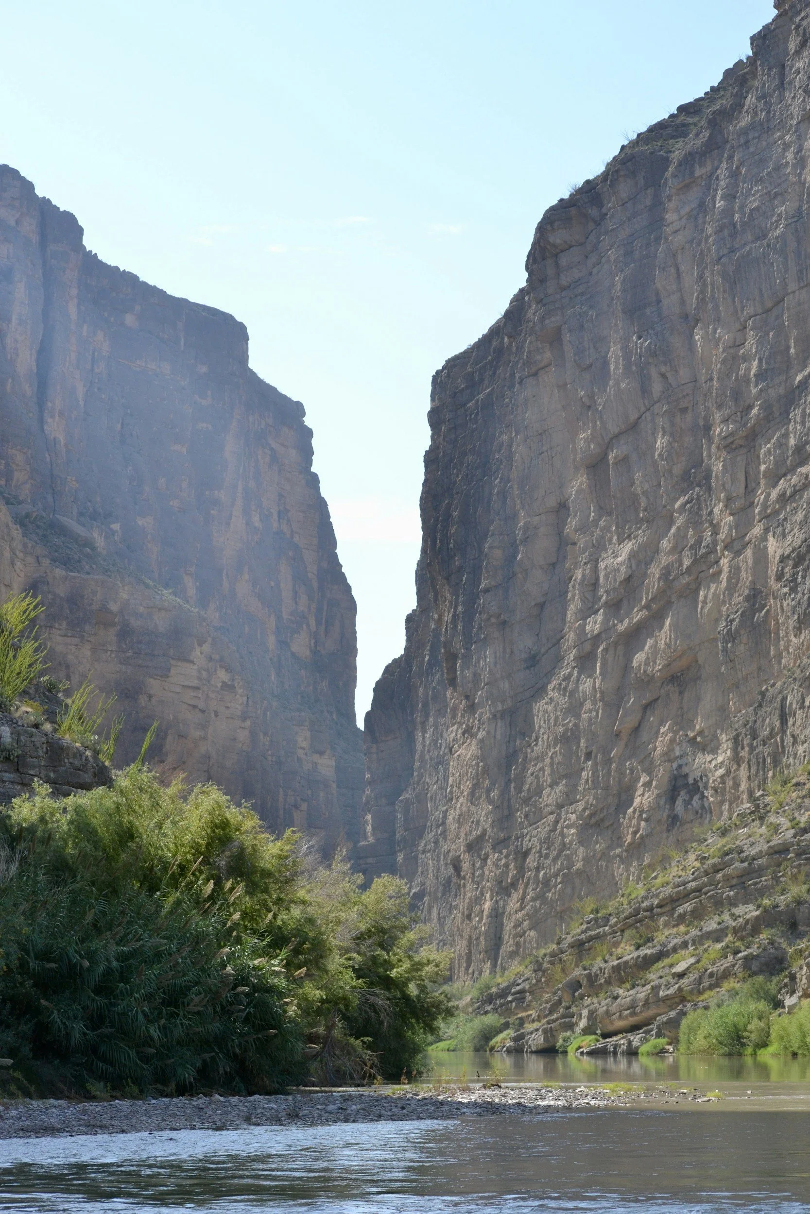 A river flowing through a Texas canyon with tall rock cliffs on either side and green vegetation along the riverbank.