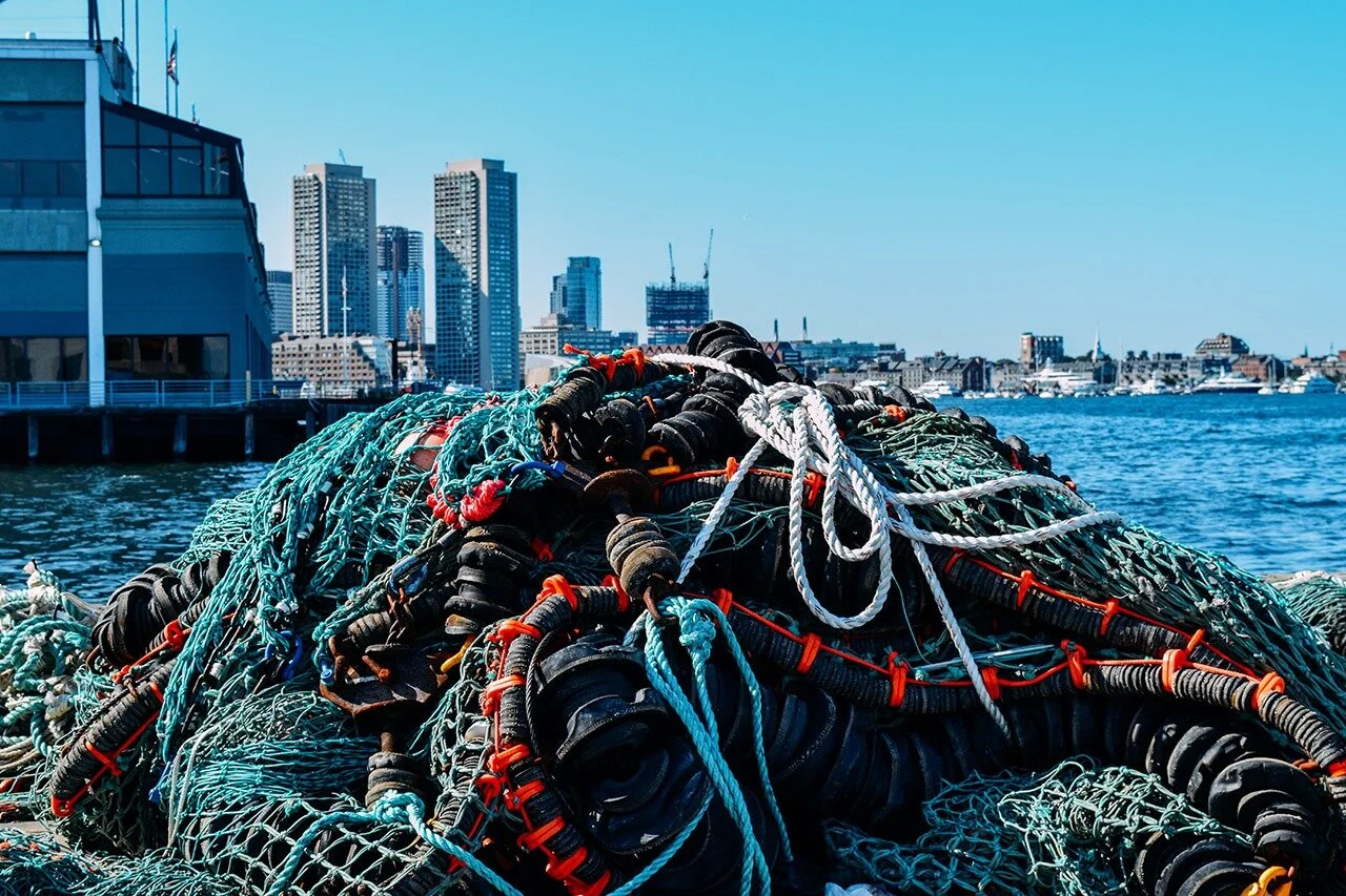  A pile of fishing nets and lines sits on the dock with the ever growing Seaport skyline sparkling in the background.   