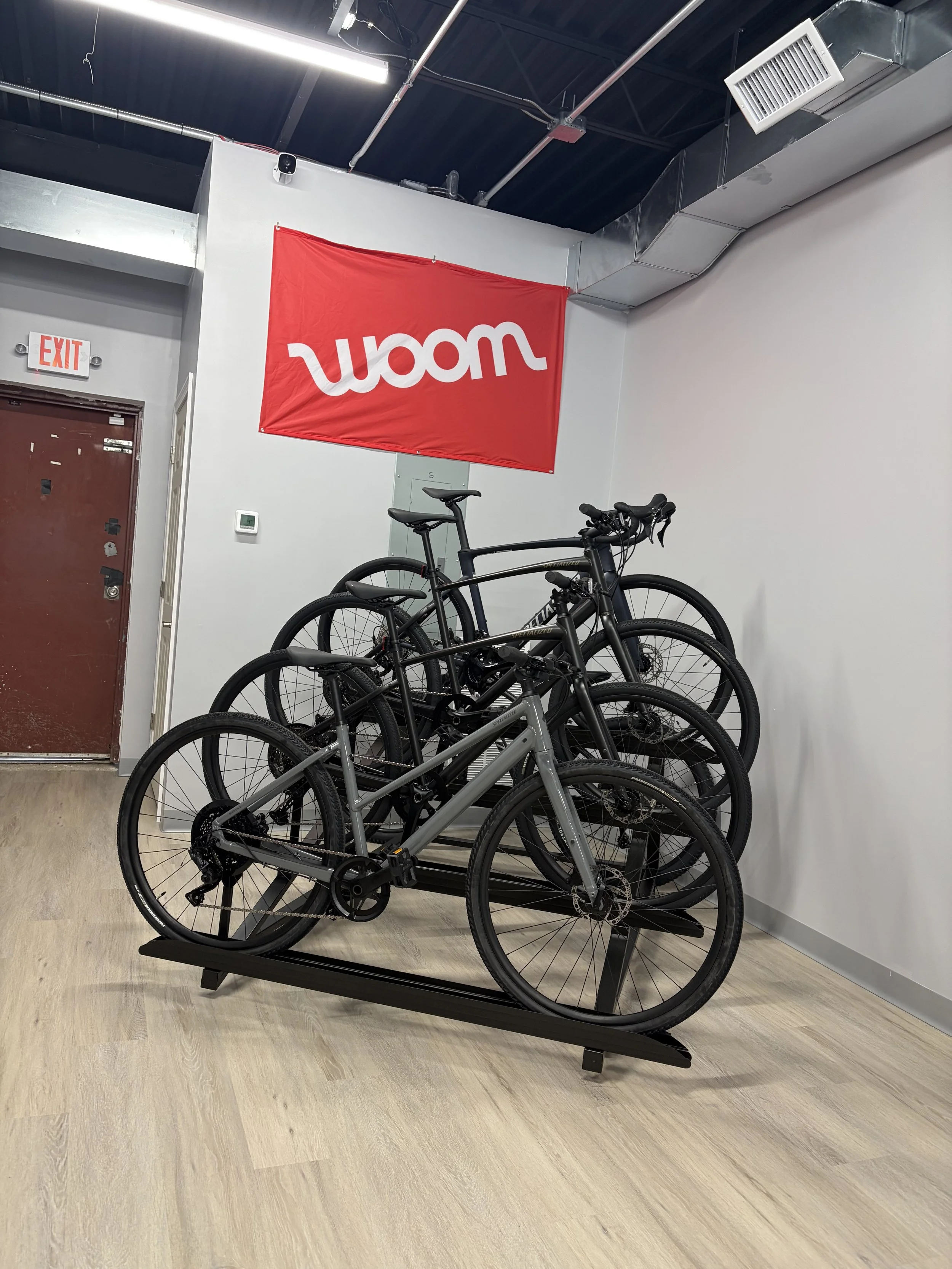 Several Specialized bicycles displayed on a rack beneath a red Woom banner inside a bike shop