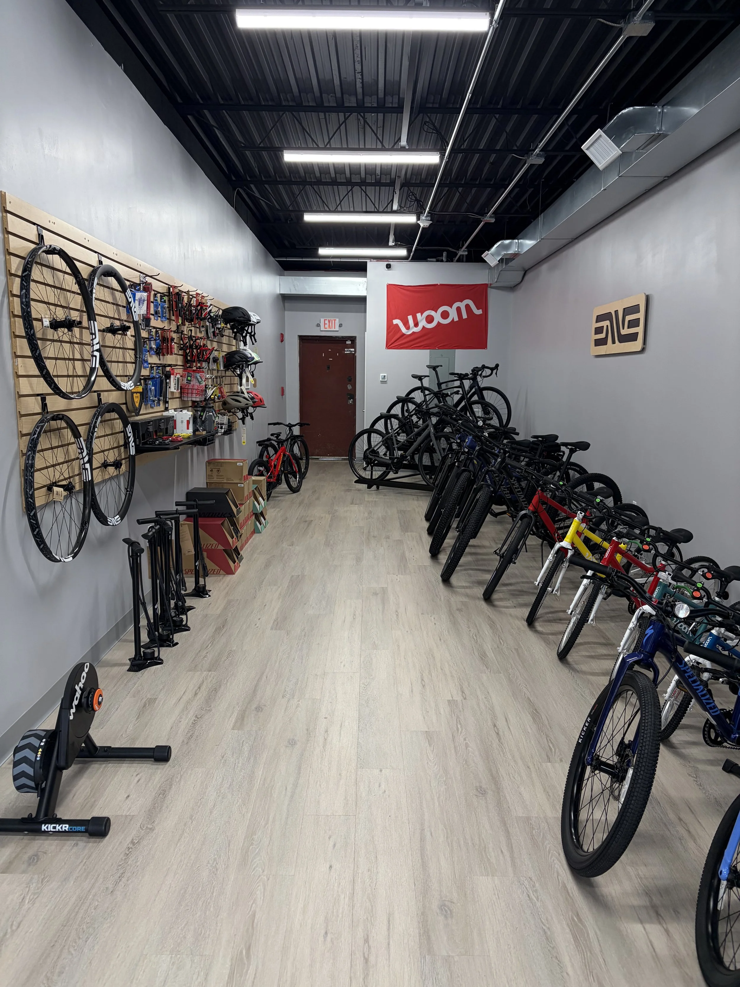 Interior of a bicycle shop displaying bikes, wheels, cycling accessories, helmets, and indoor trainers.