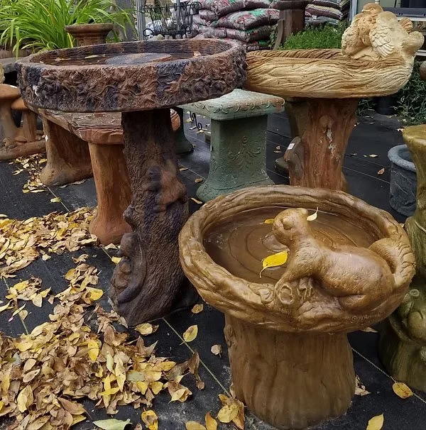 Displays outdoor garden ornaments, including tree-stump-like tables and animal-themed birdbaths, with fallen leaves on the ground.