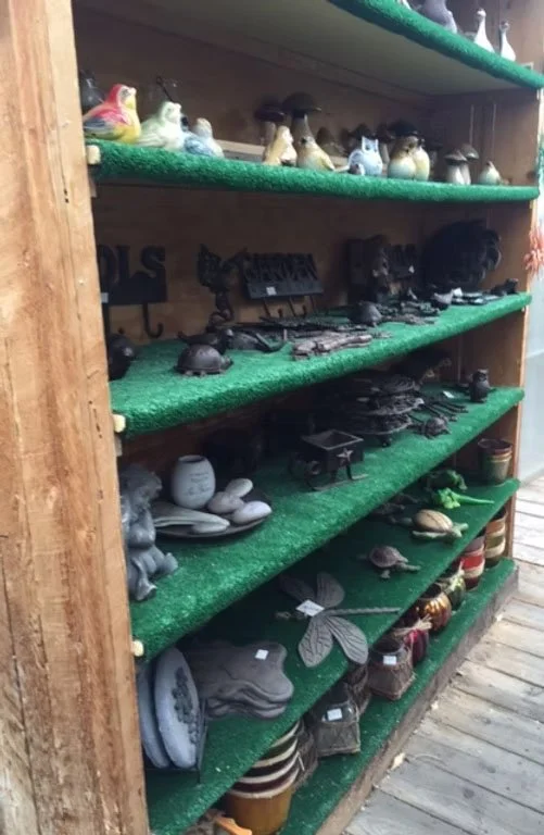 Wooden shelving unit with green carpeted shelves displaying various garden and outdoor decorations including animal figurines, lanterns, small sculptures, and planters.