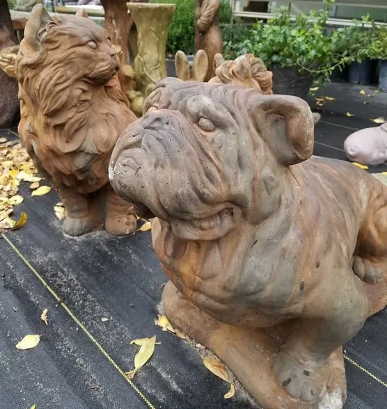 Garden display of stone animal statues including a lion and a bulldog, with other statues and plants in the background.