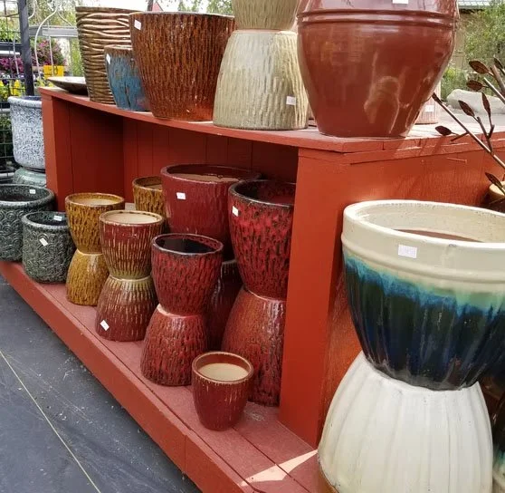 A display of various colorful ceramic flower pots on a red wooden shelf at a garden center