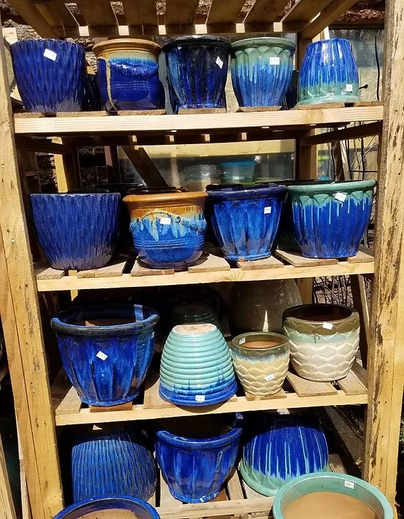 Various glazed ceramic pots in shades of blue, green, and beige displayed on a wooden shelving unit.