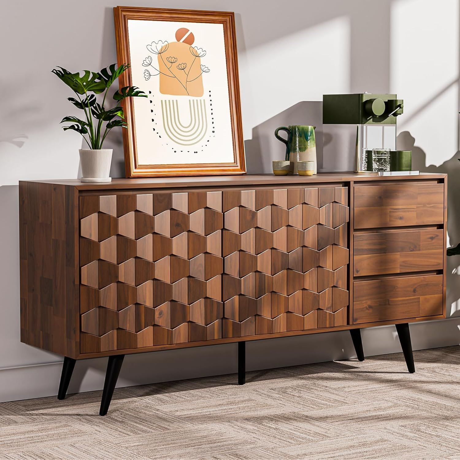 A mid-century modern wooden sideboard with a textured hexagonal pattern on the front, black angled legs, and a top decorated with a framed abstract artwork, green potted plants, a ceramic jug, and a modern green table lamp.