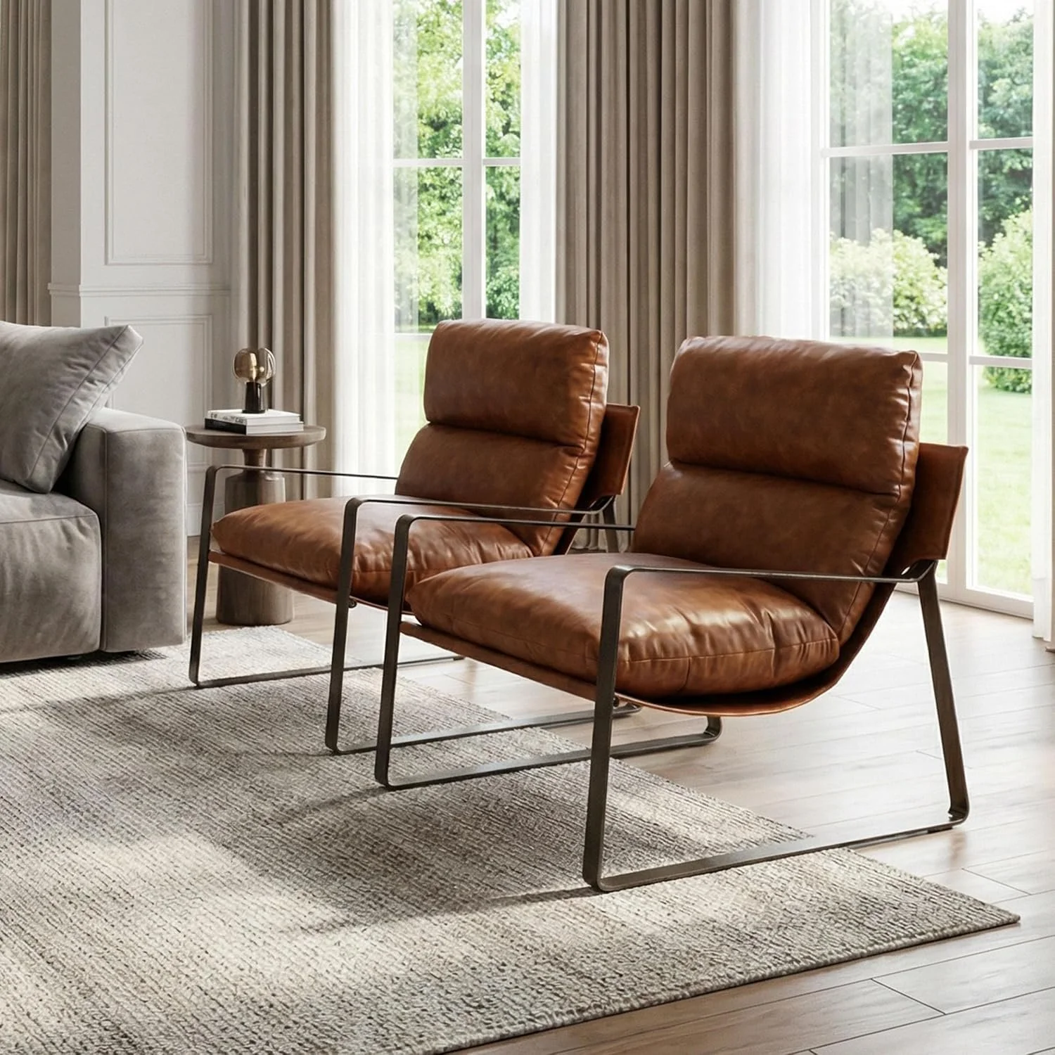 Living room with two brown leather mid-century lounge chairs, a light grey sofa, a small side table with a lamp, large windows with white curtains, and a view of green trees outside.