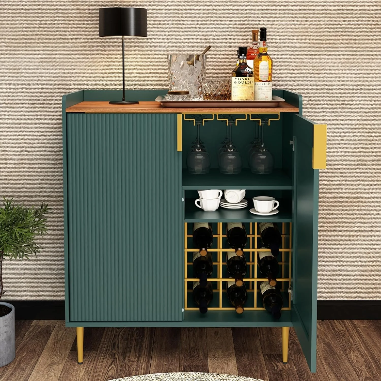 A mid-century modern bar cabinet with a closed side and an open side displaying glasses, cups, and wine bottles, topped with a tray of liquor bottles, a ice bucket, and a cocktail shaker, placed against a textured wall.