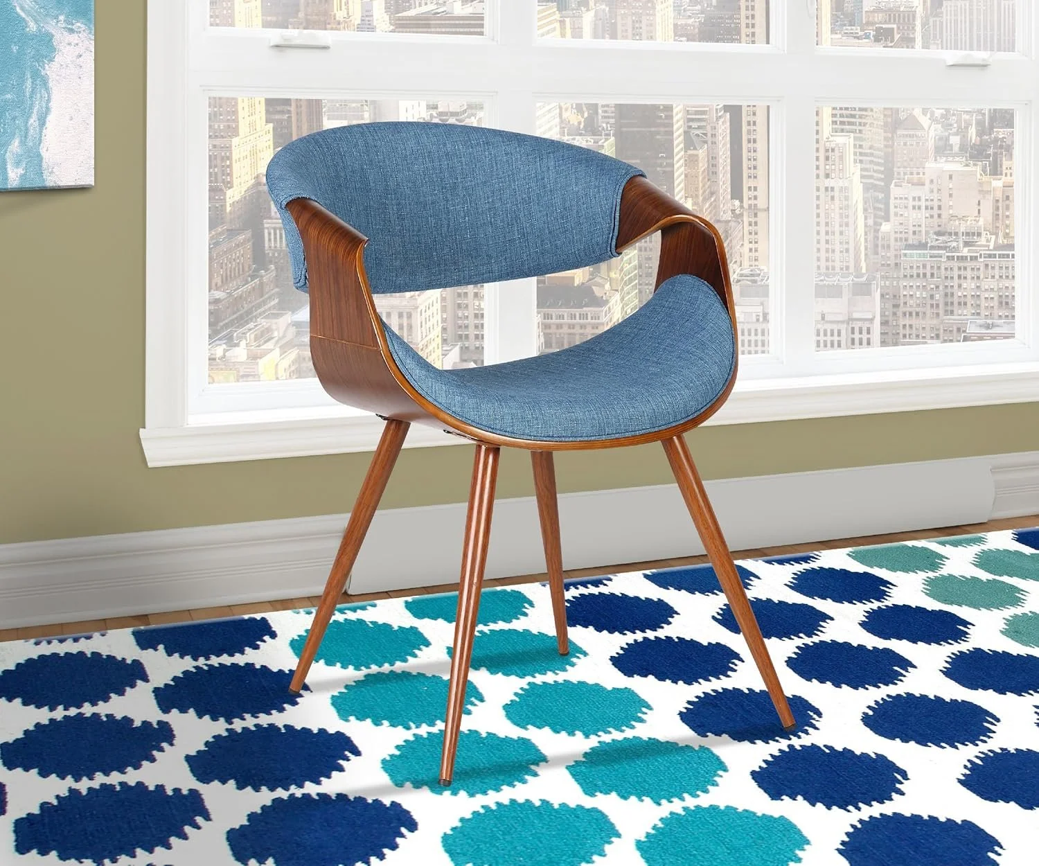A mid-century modern chair with a wooden frame and blue fabric cushions is placed in front of a large window with a cityscape view, and a blue and green patterned rug on a wooden floor.