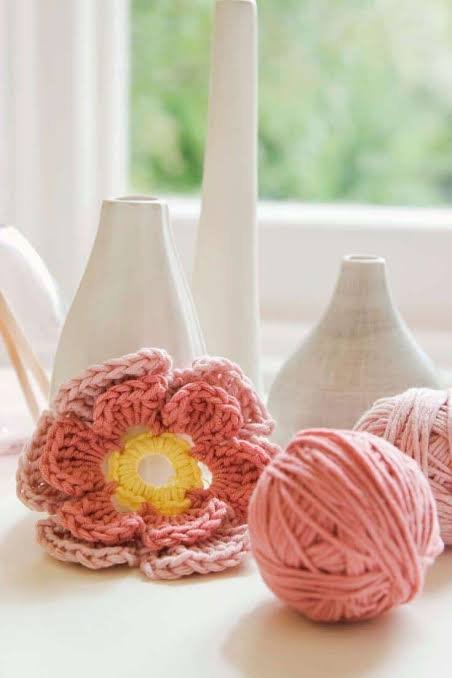 Decorative vases and balls of pink yarn on a table near a window.