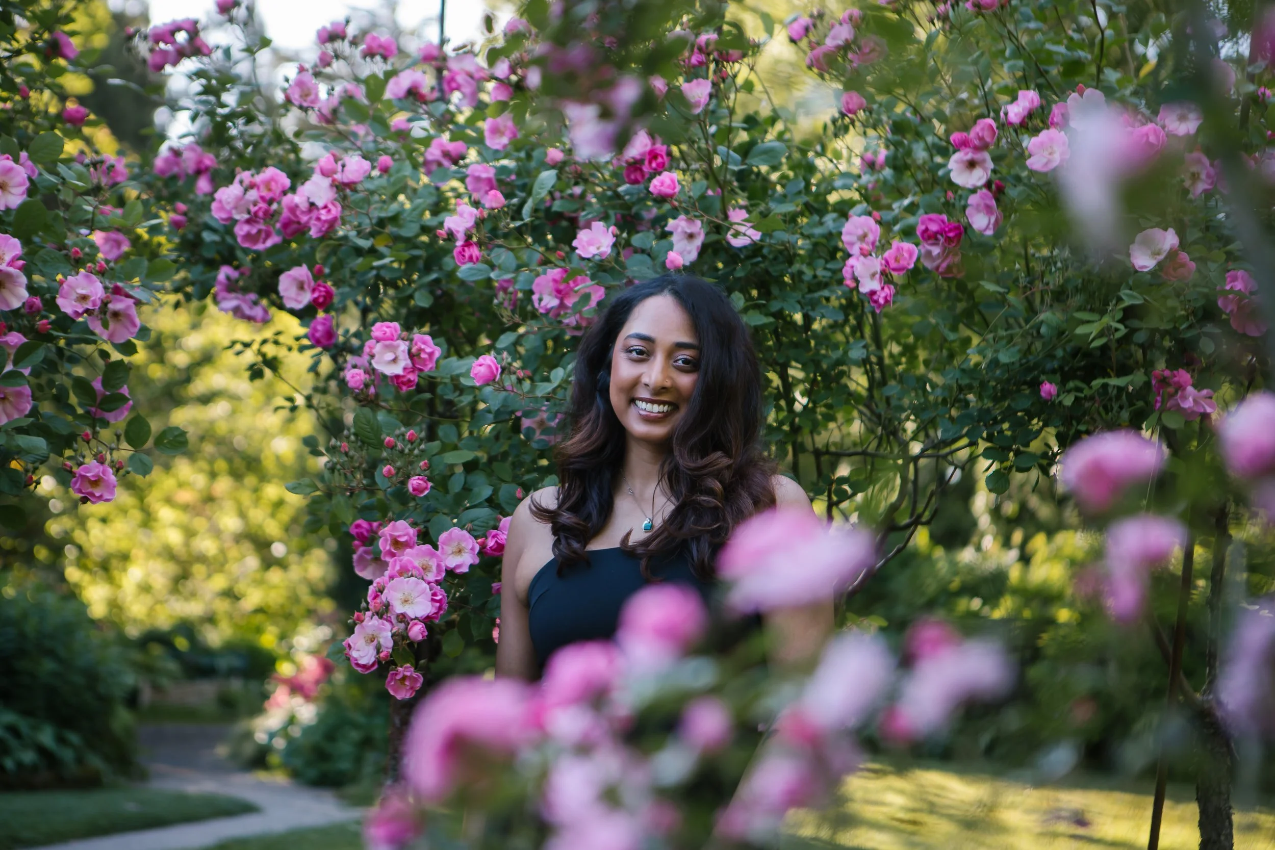 A woman standing among pink and white blooming flowers in a garden.
