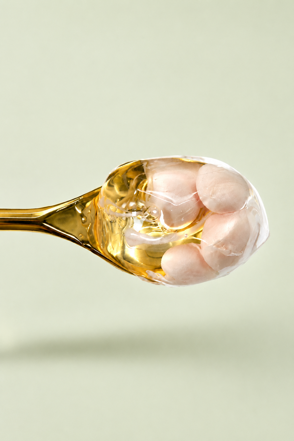 Close-up of a spoon filled with translucent oil and seafood, possibly scallops, on a light green background.