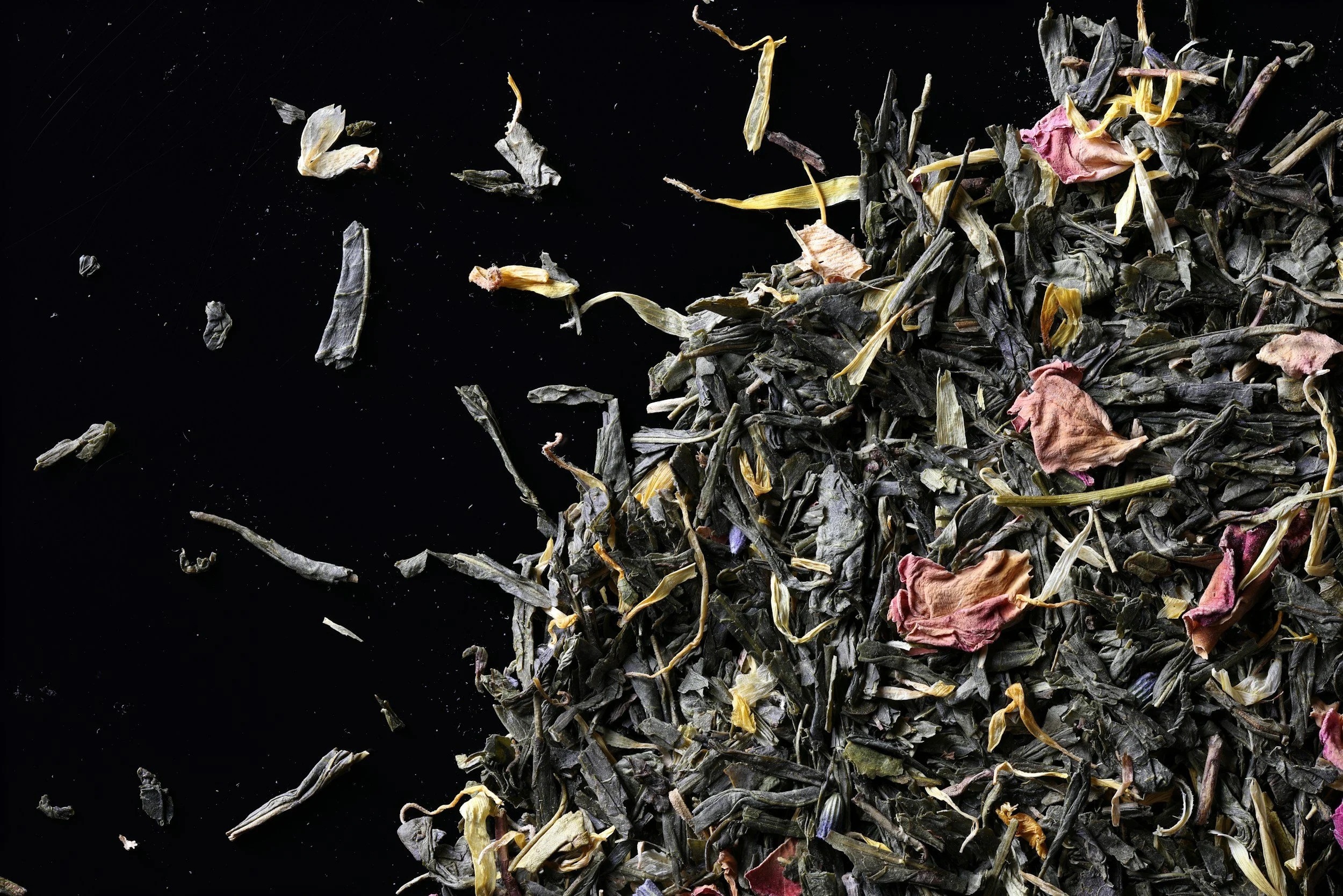 Close-up of a pile of dried loose leaf tea with flower petals on a black background.