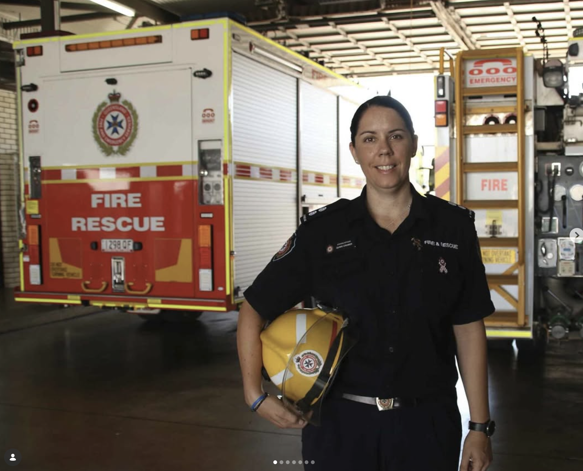 Firefighter standing in front of fire rescue truck holding a yellow helmet.