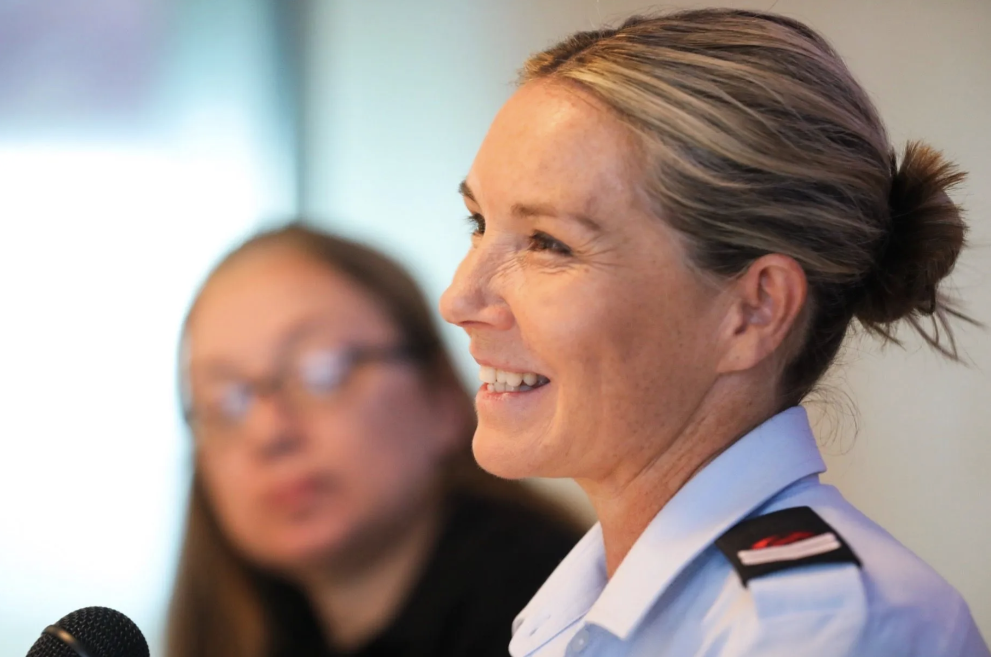 Close-up of smiling woman in uniform with a child and microphone in the foreground