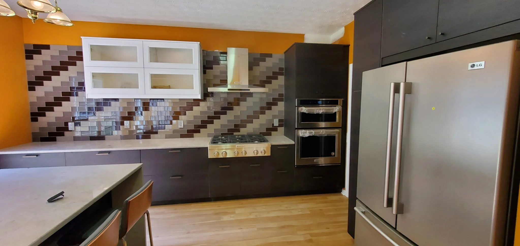 Kitchen with orange walls, white upper cabinets, dark lower cabinets, a gray and brown tile backsplash, stove, oven, microwave, and stainless steel refrigerator.
