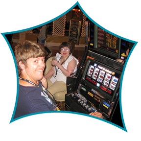 Two women sitting at a table with a slot machine in front of them inside a casino, smiling and engaged in conversation.