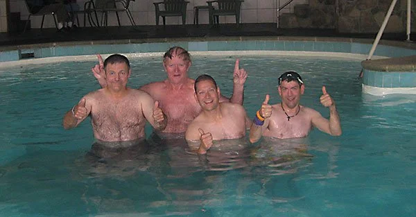 Four men in a swimming pool celebrating, with some making peace signs and thumbs up.
