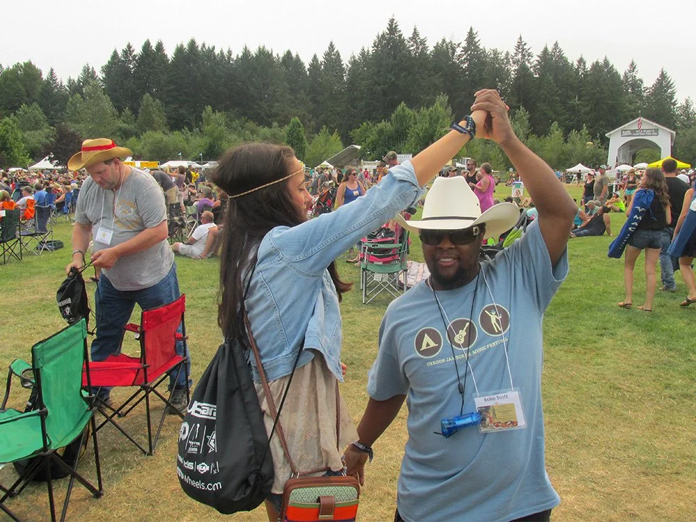 A man and woman dancing together at an outdoor festival, with many people and tents in the background.