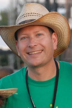 Smiling man wearing a cowboy hat and a green shirt outdoors.