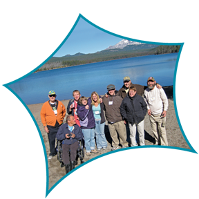 Group of people posing outdoors by a lake with mountains in the background
