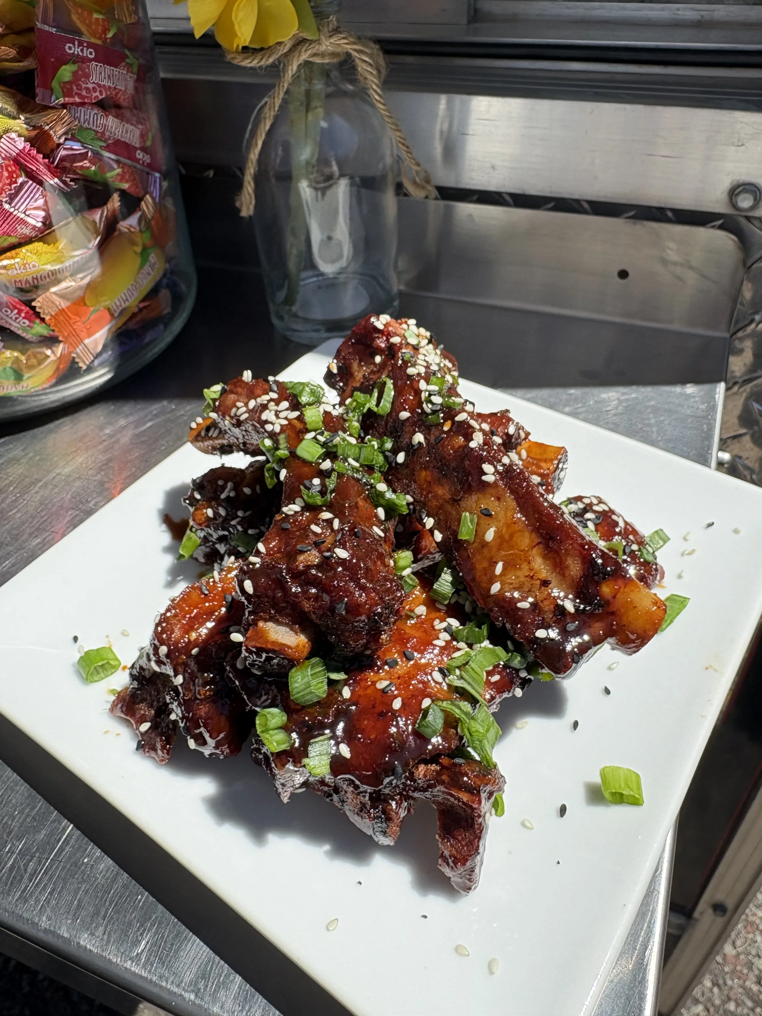 Close-up of barbecued ribs topped with chopped green onions and sesame seeds on a white plate.