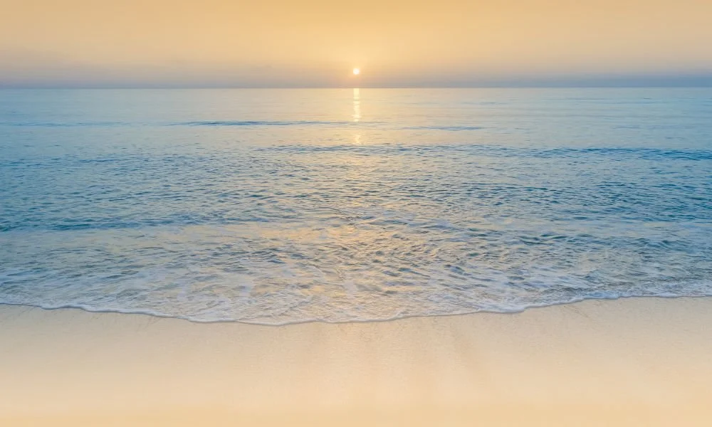 Sunset over calm ocean waters with gentle waves and sandy beach