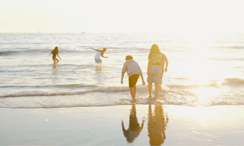People enjoying a sunny day at the beach, walking and playing in the shallow water.