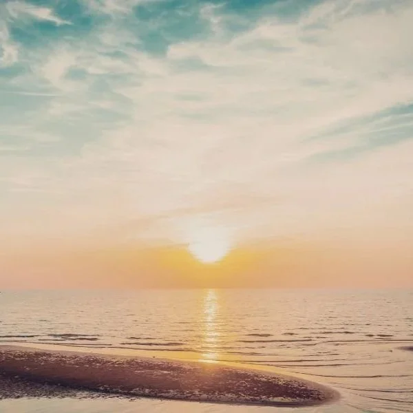 Sunset over the ocean with calm waves and a sandy beach in the foreground.