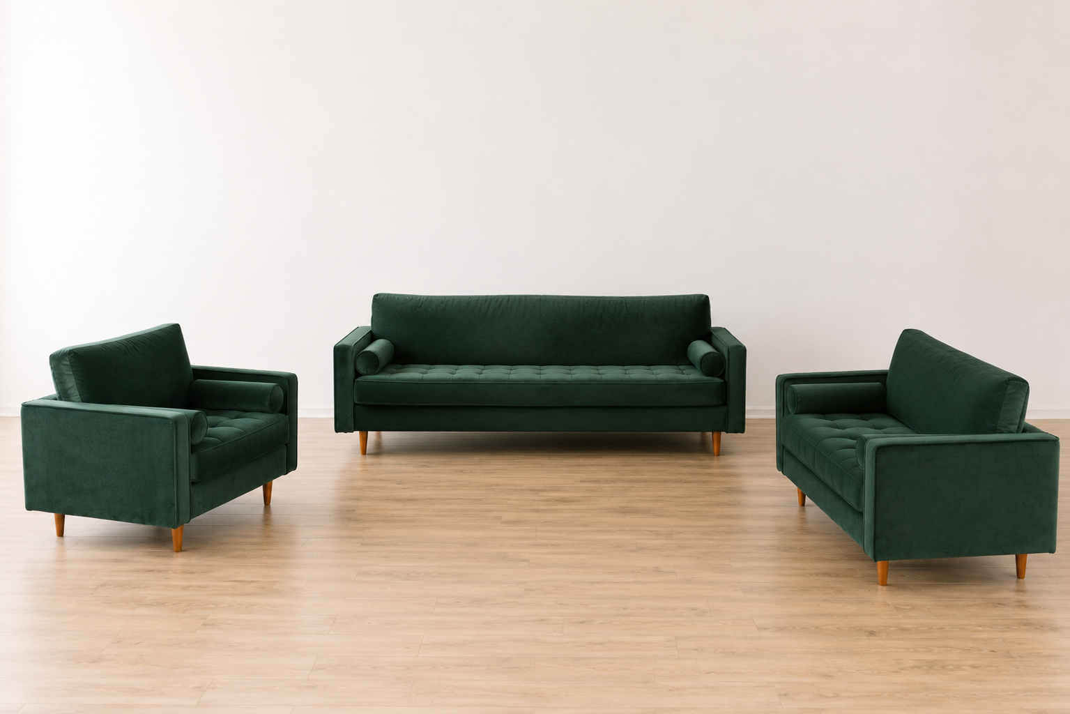 Three green velvet sofas with wooden legs arranged in a room with a light wood floor and a plain white wall.