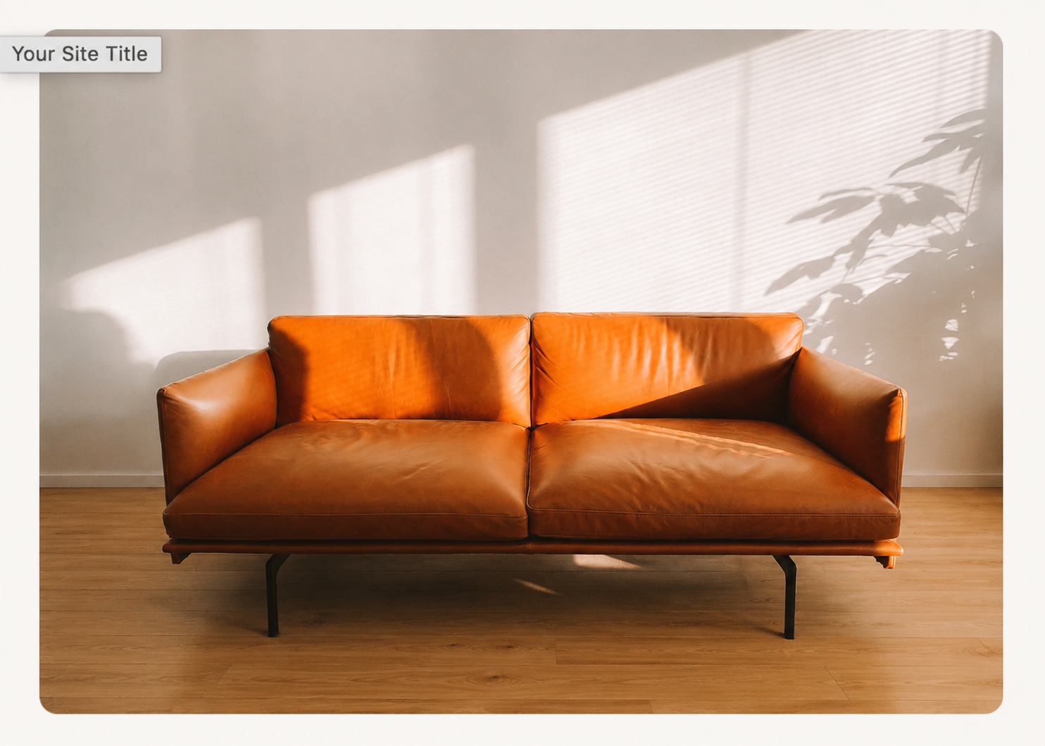 A brown leather sofa with black metal legs placed on a wooden floor, with sunlight and shadows from a window and plant projected onto the wall behind it.