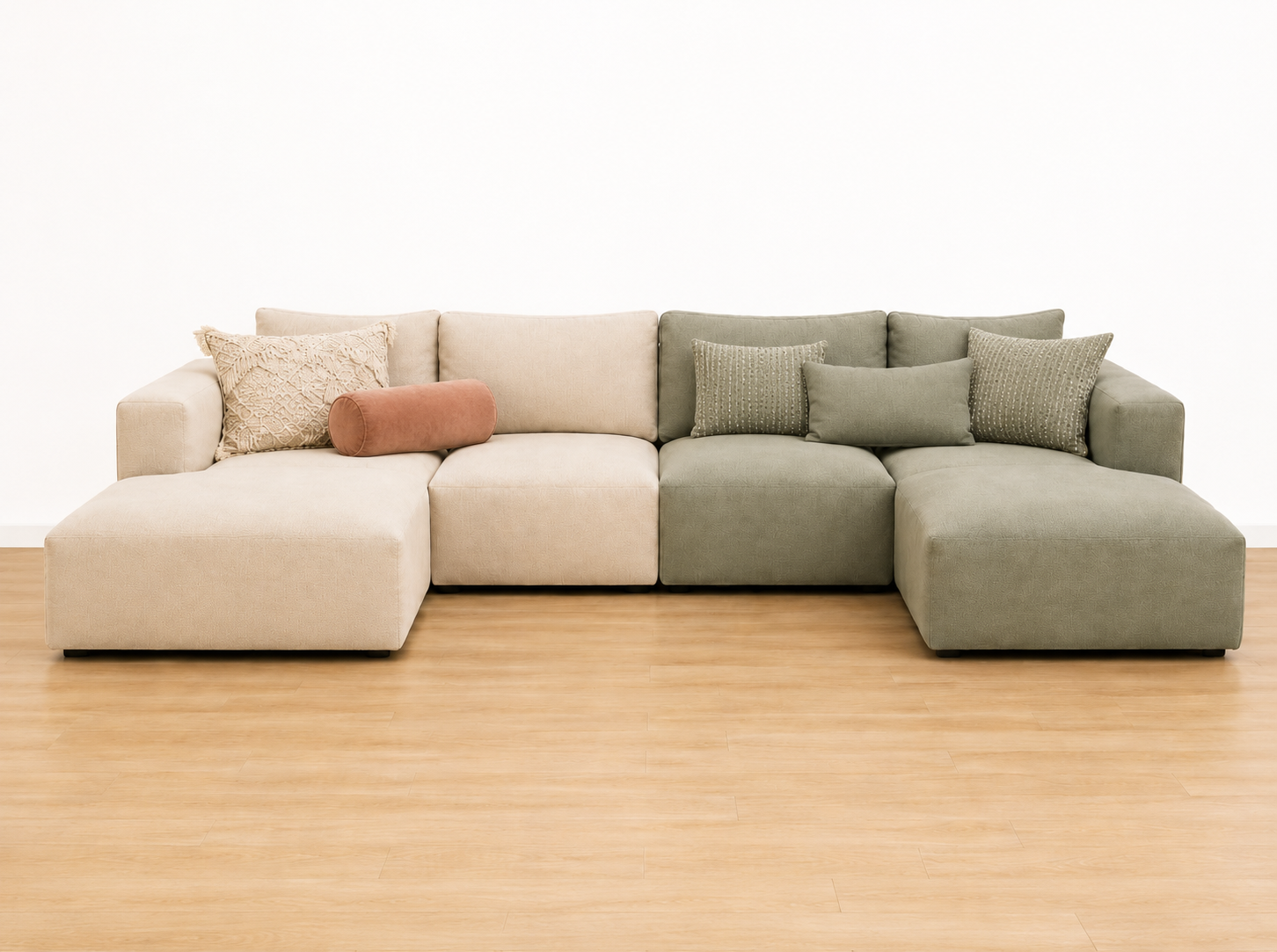 A sectional sofa with beige and light green cushions and throw pillows on a wooden floor against a white wall.