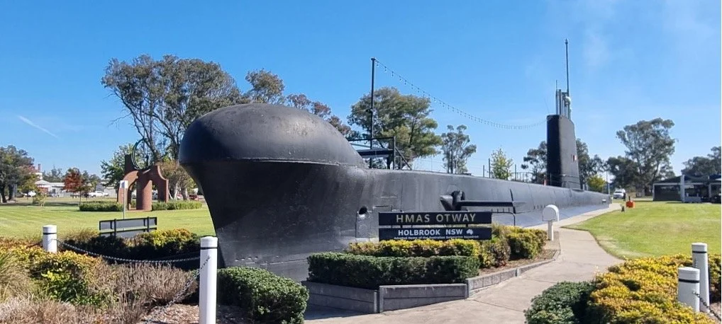 A submarine displayed outdoors in a park with trees, bushes, and a walking path