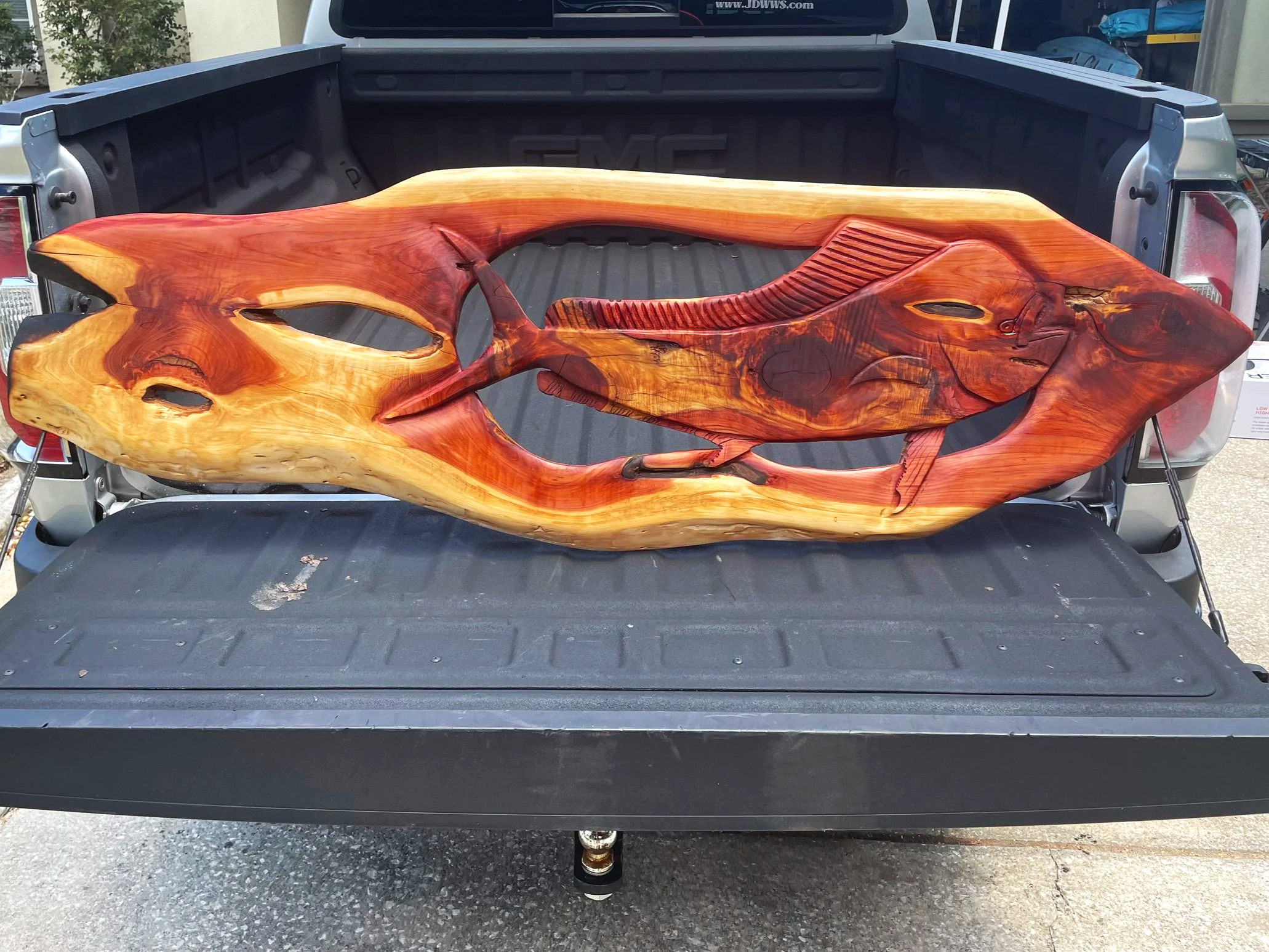 A large, detailed wooden fish sculpture lying in the bed of a pickup truck.