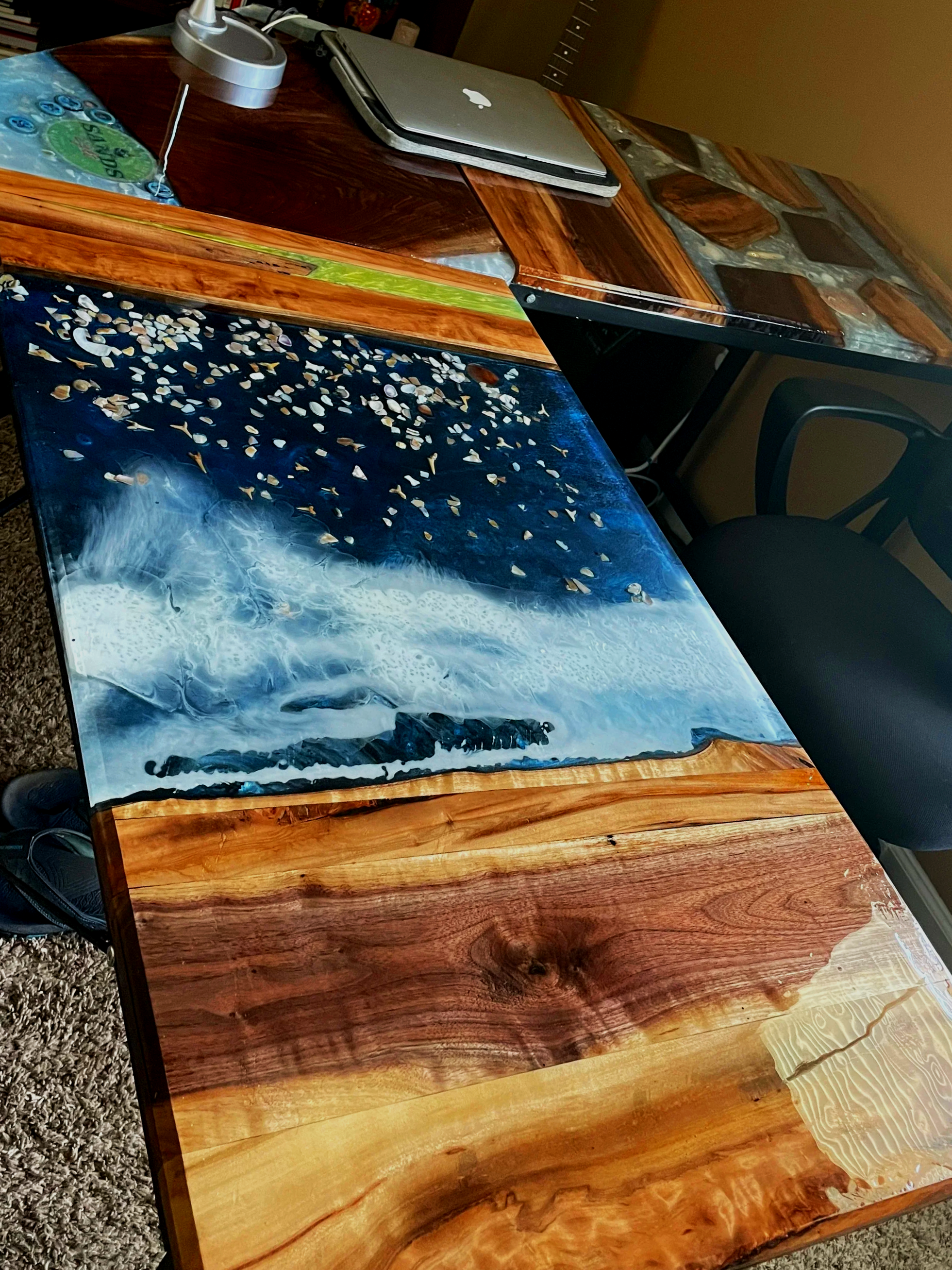 Close-up view of a wooden desk with a natural finish, displaying various wood grain patterns and colors, with some decorated and resin-embedded sections.