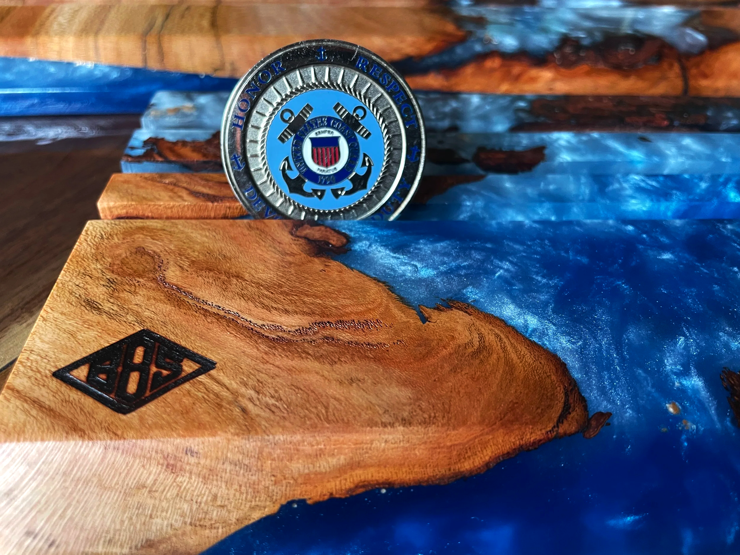 Close-up of a metallic badge or emblem with an anchor and a shield, placed on a wooden surface with a decorative blue resin inlay.