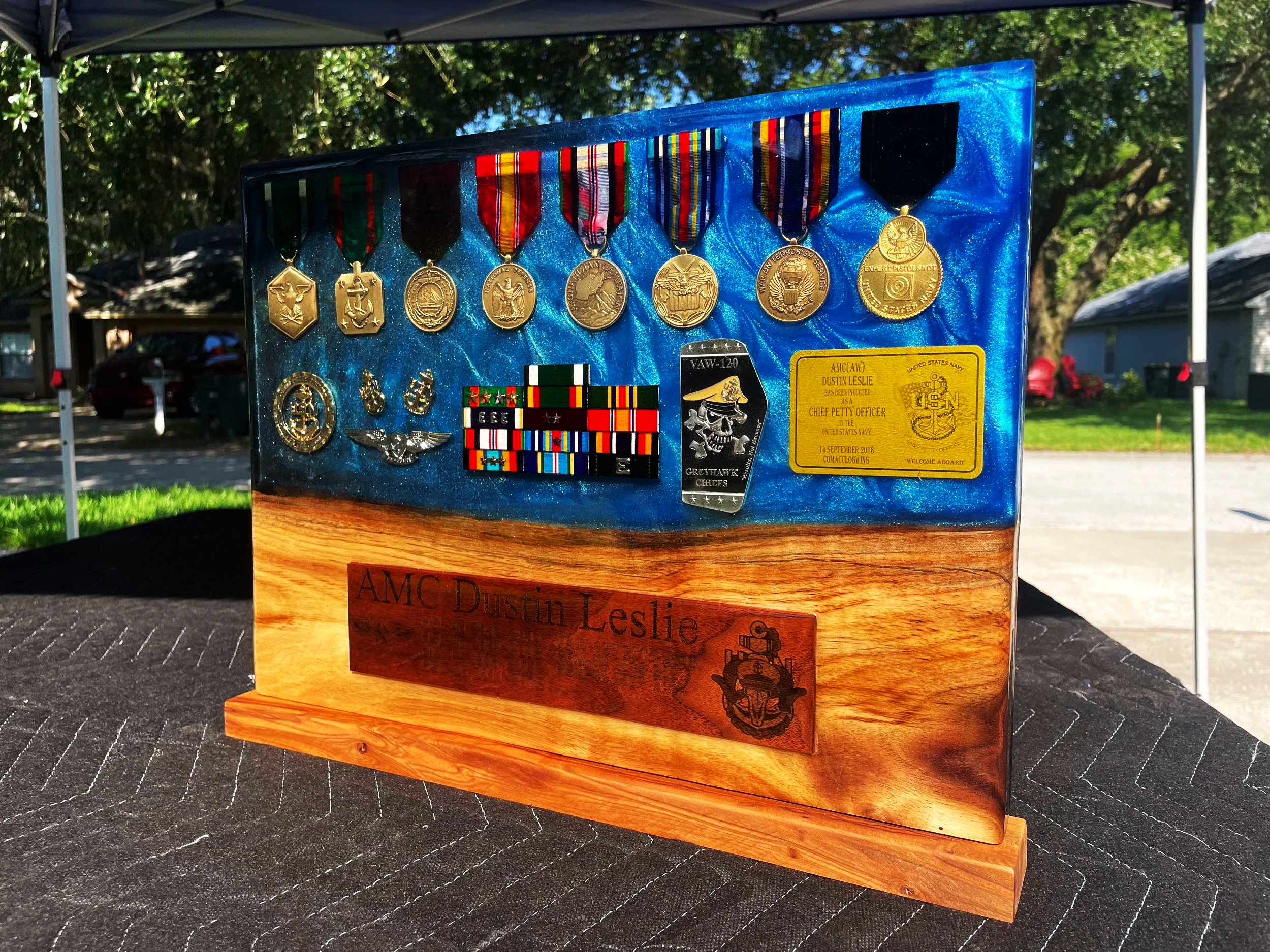 A display case showing numerous military medals, patches, and badges on a blue background at an outdoor event.