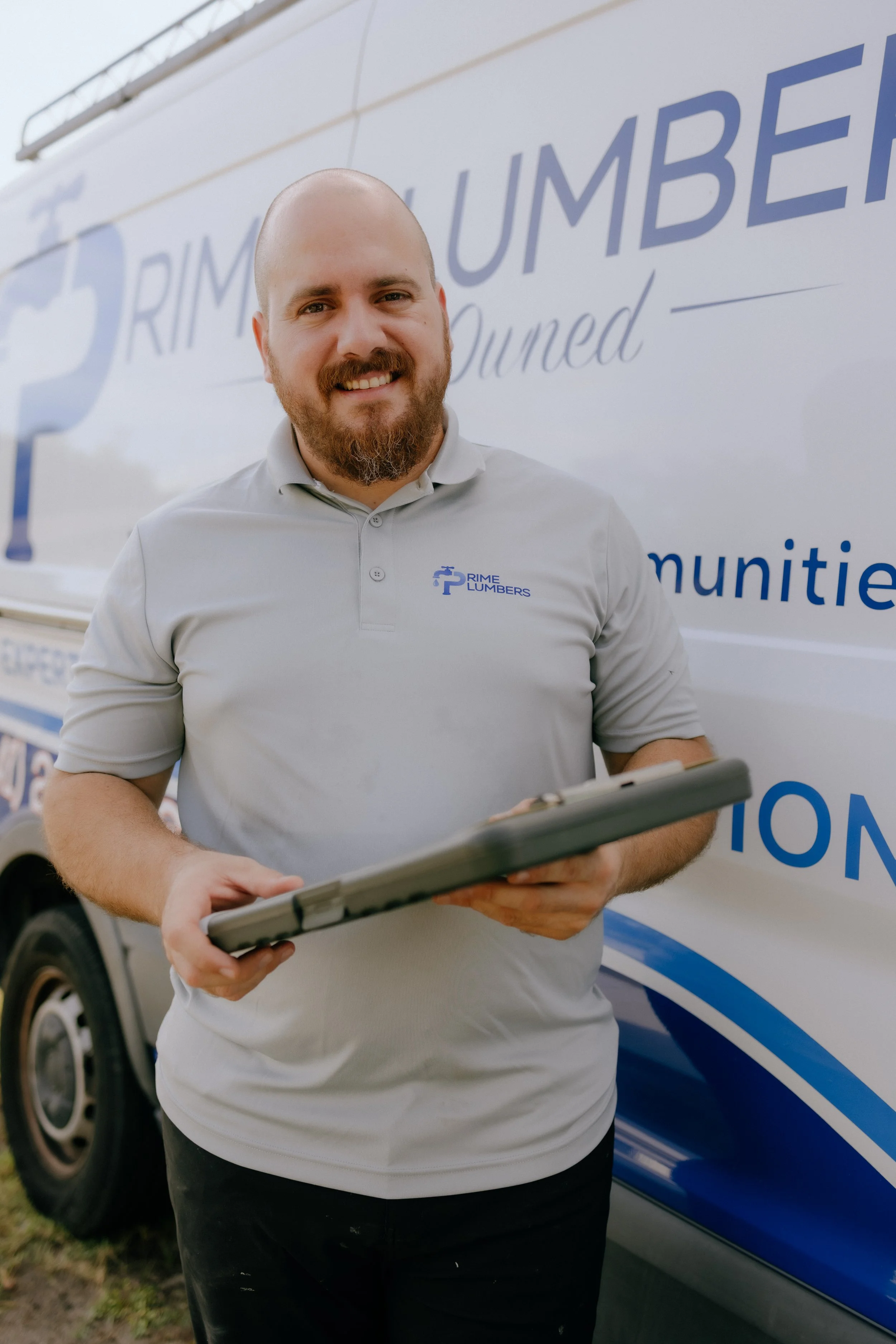 A man with a beard and a shaved head smiling and holding a clipboard in front of a Rime Bumper truck.