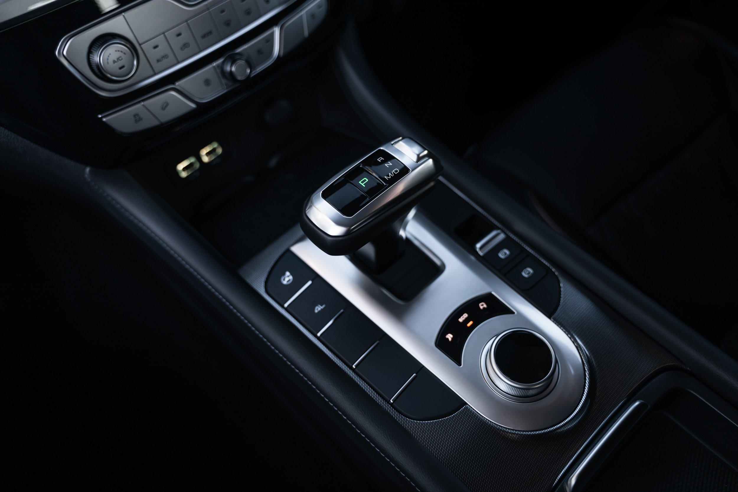 Close-up of a car gear shifter with 'P', 'R', 'N', and 'D' labels, surrounded by various control buttons, in a modern car interior.