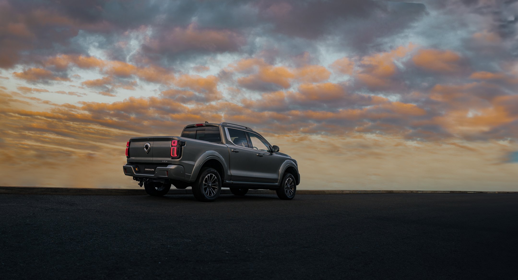 A dark gray pickup truck parked on an empty road at sunset with a partly cloudy sky in the background.