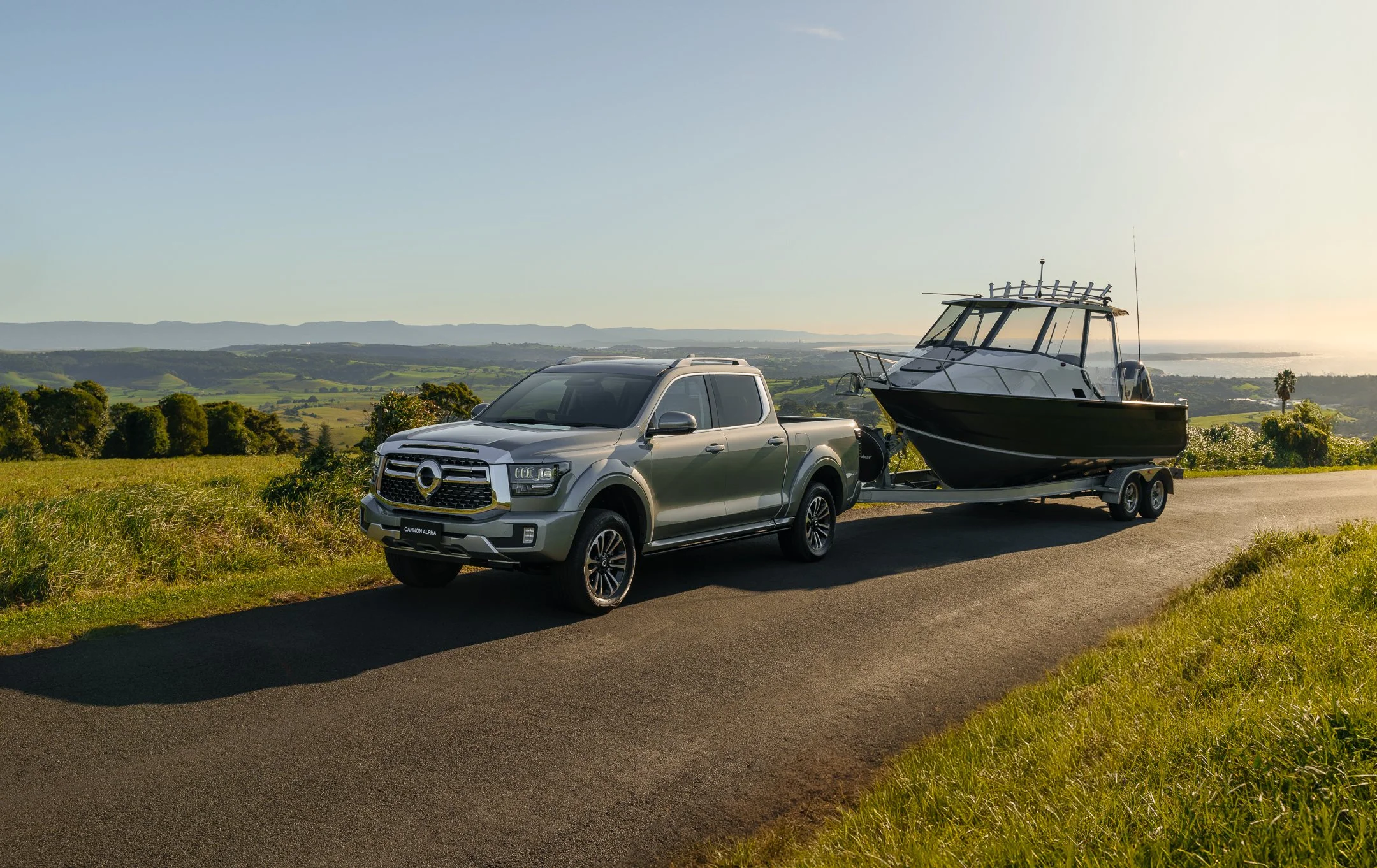 A silver pickup truck on a road, towing a boat on a trailer with a scenic landscape and distant mountains in the background.