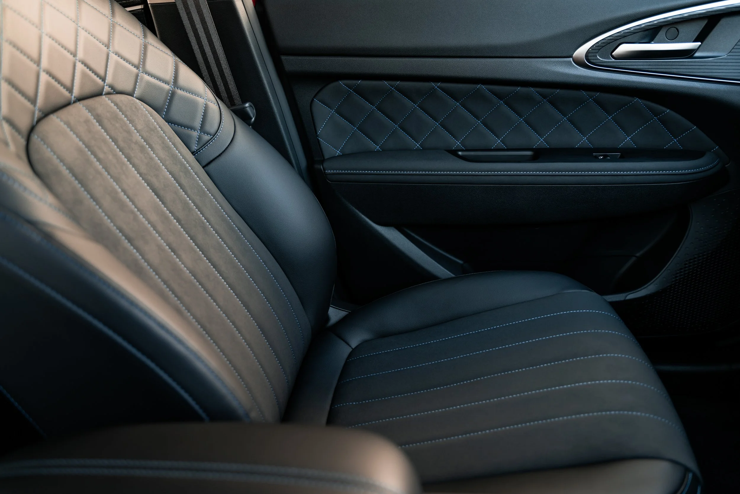 Close-up of the interior of a luxury vehicle, focusing on the black leather seats with blue stitching and diamond pattern design.